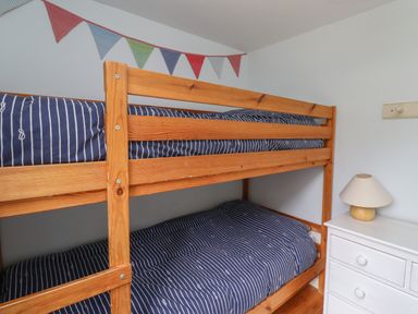 A wooden bunk bed with blue striped bedding and a chest of drawers with a lamp in a bedroom at Beachward in Embleton