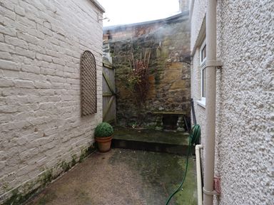 A small outdoor courtyard with stone and brick walls a potted plant hosepipe and a stone bench at Hardys House in Alnwick