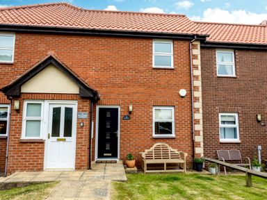 A brick house exterior with two doors wooden bench and garden at The Apartment in Bamburgh