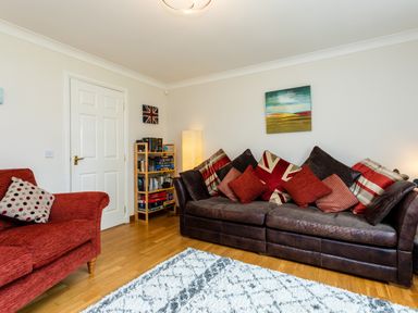 A living room with a brown leather sofa with cushions and a red armchair at The Apartment in Bamburgh
