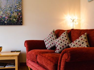 A red sofa with three polka dot cushions next to a wooden side table with books and a bowl at The Apartment in Bamburgh