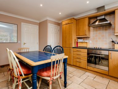 A kitchen with wooden cabinets a blue tile dining table with four chairs and a built in oven at The Apartment in Bamburgh