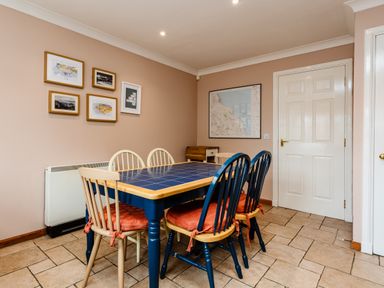 A dining area with a blue tile table and six chairs with cushions and framed pictures on the wall at The Apartment in Bamburgh