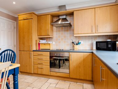 A kitchen with wooden cabinets a stainless steel oven a microwave and a blue chair at The Apartment in Bamburgh