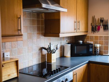A kitchen counter with a stove microwave cooking utensils and knives on the wall at The Apartment in Bamburgh