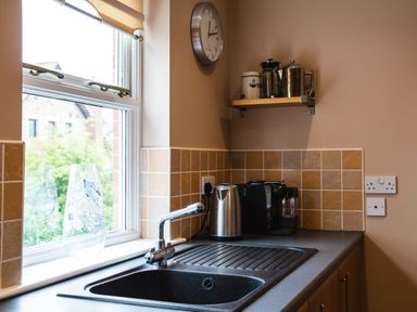 A kitchen sink below a window with a glass vase a kettle coffee machine and canisters on the countertop at The Apartment in Bamburgh