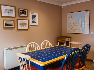 A dining room with a blue tiled table and mixed chairs with framed pictures on the wall at The Apartment in Bamburgh