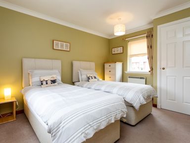 A bedroom with two single beds nightstand with lamp chest of drawers window and door at The Apartment in Bamburgh