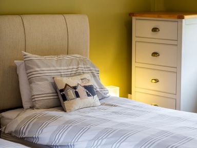 A bedroom with a bed with striped bedding and a decorative pillow next to a white dresser at The Apartment in Bamburgh
