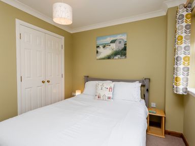 A bedroom with a double bed white bedding a small wooden bedside table a closet with white doors and patterned curtains at The Apartment in Bamburgh