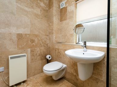 A bathroom with a wall-mounted toilet sink a radiator and a window at The Apartment in Bamburgh
