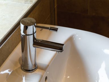 A chrome faucet attached to a white ceramic sink with a beige countertop and tiled wall at The Apartment in Bamburgh