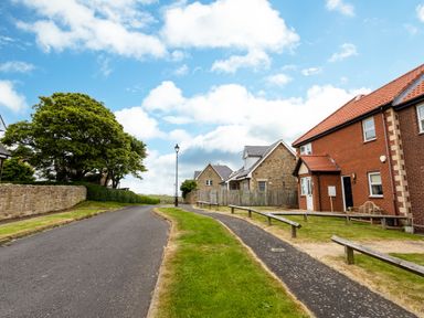 A residential street with houses a tree lamp posts and a paved road at The Apartment in Bamburgh