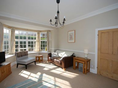 A living room with a brown sofa a small chair wooden side tables a lamp a TV and large windows at Beach House (Alnmouth) in Alnmouth