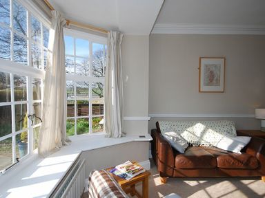 A living room with a brown leather sofa near a large bay window with curtains at Beach House Alnmouth