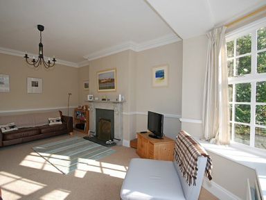 A living room with a sofa a fireplace a television and a window with curtains at Beach House (Alnmouth) in Alnmouth