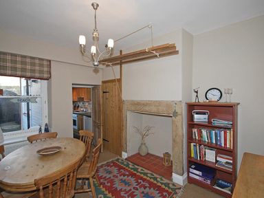 A dining room with a wooden table and chairs a bookshelf a fireplace and a window with a beach sign at Beach House (Alnmouth) in Alnmouth