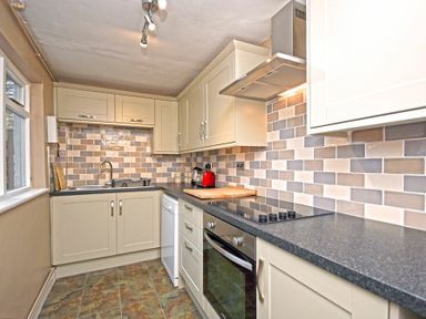 A kitchen with cream cabinets black countertop tiled backsplash and various appliances at Beach House (Alnmouth) in Alnmouth