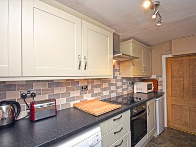A kitchen with white cabinets black countertop red toaster and kettle chopping board oven microwave and wooden door at Beach House (Alnmouth) in Alnmouth