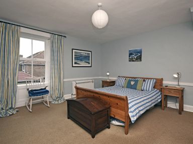 A bedroom with a wooden bed and striped bedspread with two bedside tables and lamps at Beach House (Alnmouth) in Alnmouth