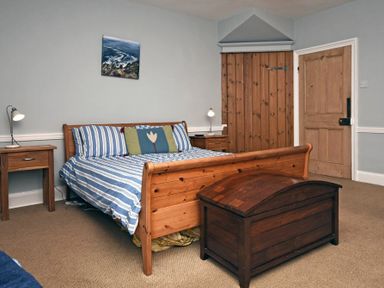 A bedroom with a wooden bed blue striped bedding wooden bedside tables lamps wooden chest and a wooden door at Beach House (Alnmouth) in Alnmouth