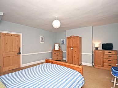 A bedroom with a wooden bed, wardrobe, chest of drawers, dressing table, and small television at Beach House (Alnmouth) in Alnmouth