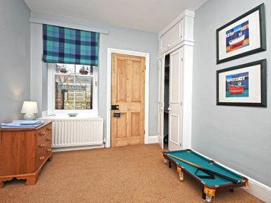 A room with a wooden door a chest of drawers with a lamp a window with a seaside sign and a small pool table on the floor at Beach House (Alnmouth) in Alnmouth