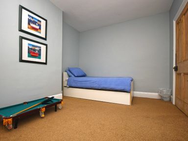 A bedroom with a single bed with blue bedding a small pool table two framed pictures on the wall and a wooden door at Beach House (Alnmouth) in Alnmouth