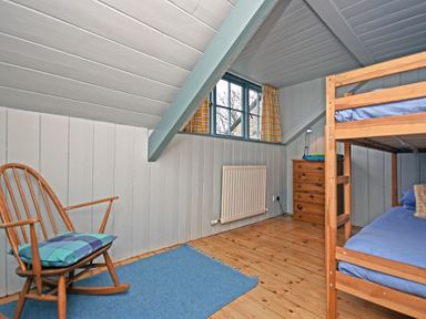 A bedroom with bunk beds a rocking chair a wooden chest of drawers and a window with curtains at Beach House in Alnmouth