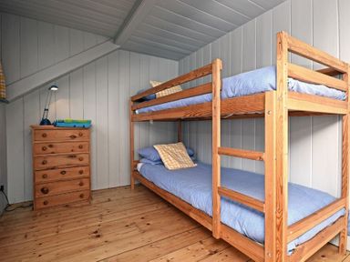 A bedroom with wooden bunk beds and a wooden dresser with a lamp and folded towels at Beach House (Alnmouth) in Alnmouth