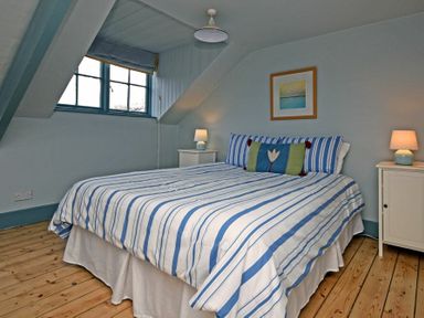 A bedroom with a double bed striped bedding two bedside tables with lamps and a window at Beach House Alnmouth