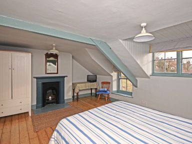 A bedroom with a bed striped in blue and white a wooden chair table with a cloth a wardrobe and a fireplace at Beach House (Alnmouth) in Alnmouth