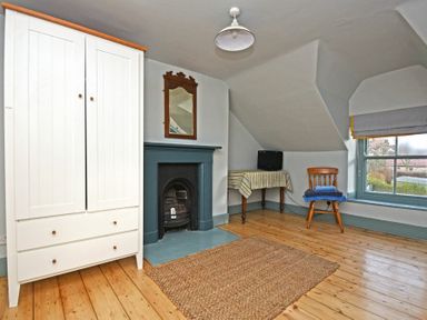 A room with wooden floor a white wardrobe a small fireplace a mirror a table with a cloth and a small television and a wooden chair with towels by a window at Beach House (Alnmouth) in Alnmouth