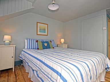 A bedroom with a double bed with striped bedding two bedside tables with lamps and a framed picture on the wall at Beach House in Alnmouth