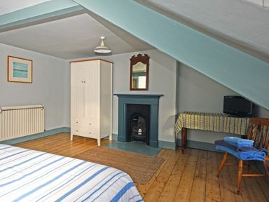 A bedroom with wooden floors a white wardrobe a small dark fireplace a table with a cloth a chair with folded towels and a small TV at Beach House in Alnmouth