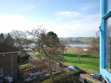 View of parked cars by a road with trees and boats on a river in the background from an open window at Beach House (Alnmouth) in Alnmouth
