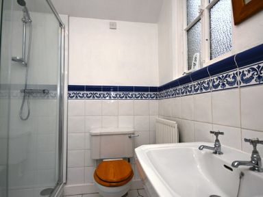 A bathroom with a shower, toilet with wooden seat, sink, and tiled walls with blue border at Beach House (Alnmouth) in Alnmouth