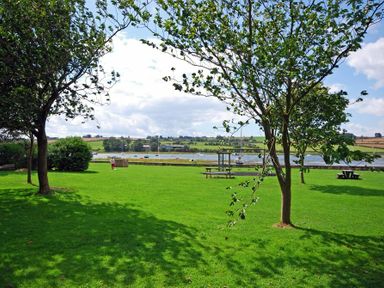 A grassy park area with trees benches and a waterfront view of boats at Beach House Alnmouth