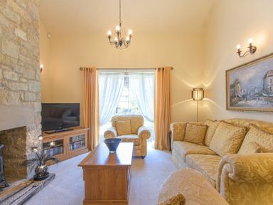 A living room with a stone fireplace a television on a wooden cabinet an armchair a sofa a coffee table and a large window with curtains at Lavender Cottage Village Farm in Seahouses