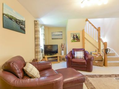 A living room with leather armchairs a television and a staircase at Lavender Cottage Village Farm in Seahouses