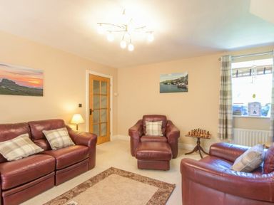 A living room with leather sofas and armchairs a chess set on a side table and photos on the wall at Lavender Cottage Village Farm in Seahouses