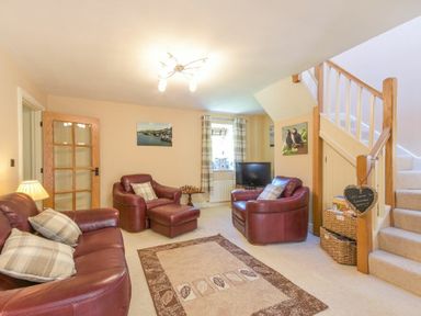 A living room with leather armchairs a sofa a rug and a staircase with baskets at Lavender Cottage Village Farm in Seahouses