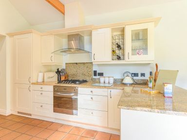 A kitchen with cream cabinets a gas stove an oven and a countertop with various kitchen items at Lavender Cottage Village Farm in Seahouses