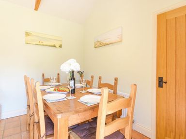A dining room with a wooden table set with plates glasses and a flower vase at Lavender Cottage Village Farm in Seahouses