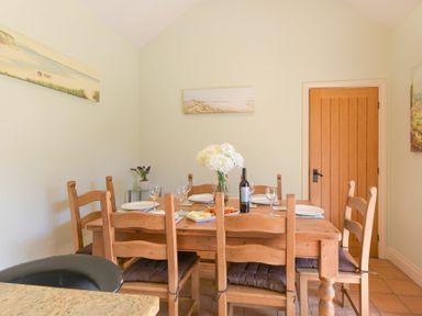 A dining room with a wooden table set with plates wine glasses and a bottle of wine at Lavender Cottage Village Farm in Seahouses