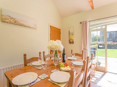 A dining room with a wooden table set for six near a glass door leading to a garden at Lavender Cottage Village Farm in Seahouses