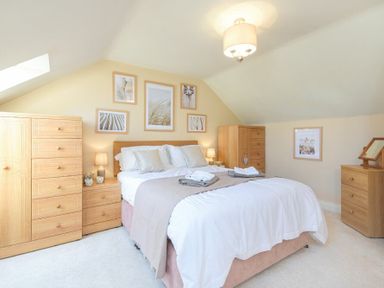 A bedroom with a double bed two wooden dressers a wooden wardrobe and framed pictures on walls at Lavender Cottage Village Farm in Seahouses