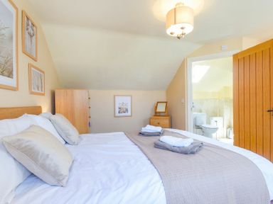 A bedroom with a double bed bedside table dresser framed pictures and an open door leading to a bathroom at Lavender Cottage Village Farm in Seahouses