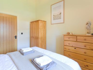A bedroom with a wooden dresser wardrobe and bed with folded towels at Lavender Cottage Village Farm in Seahouses