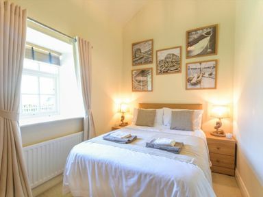 A bedroom with a bed and bedside tables with lamps and a window with curtains at Lavender Cottage Village Farm in Seahouses
